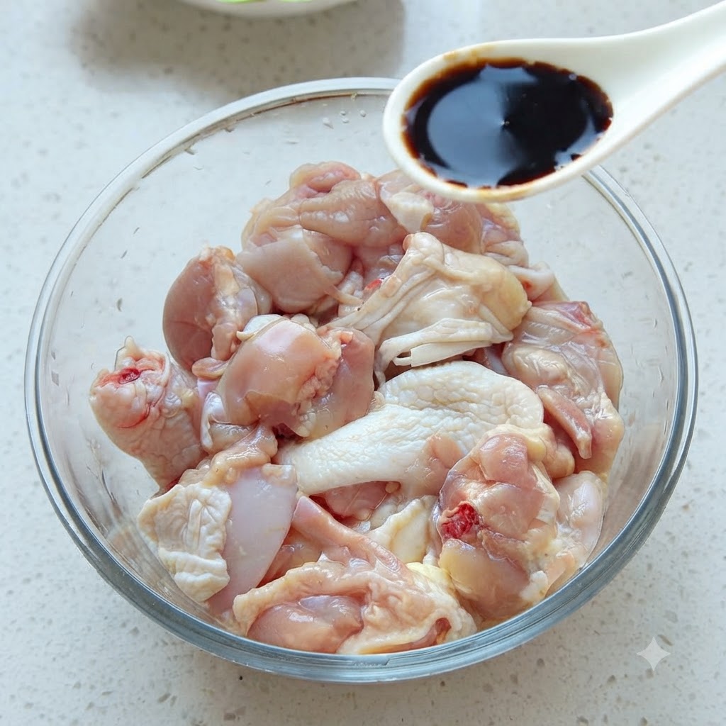 Un cucchiaio di salsa di soia scura che viene aggiunto in una ciotola di vetro piena di pezzi di pollo crudo.