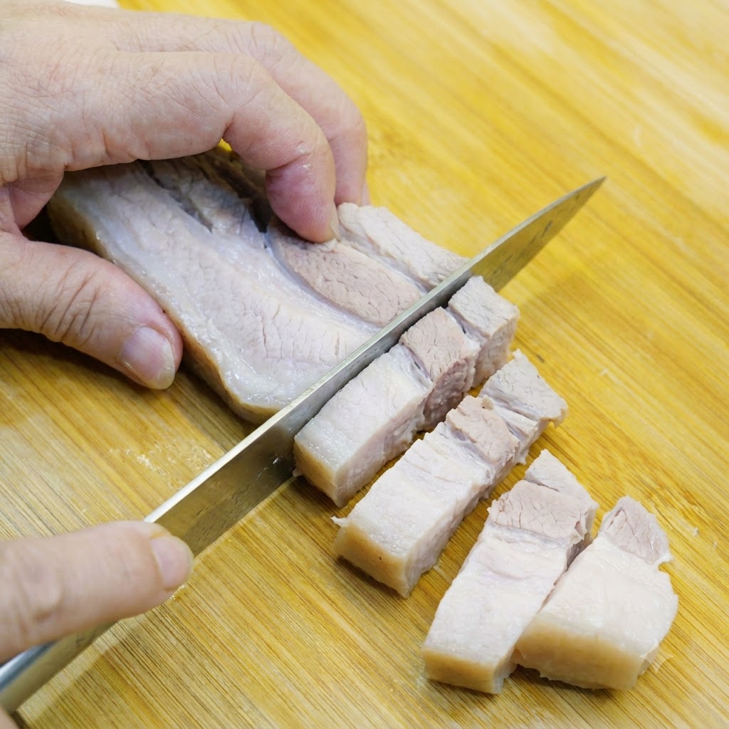 Pancia di maiale sbollentata tagliata a pezzi della dimensione di un boccone su un tagliere di legno.