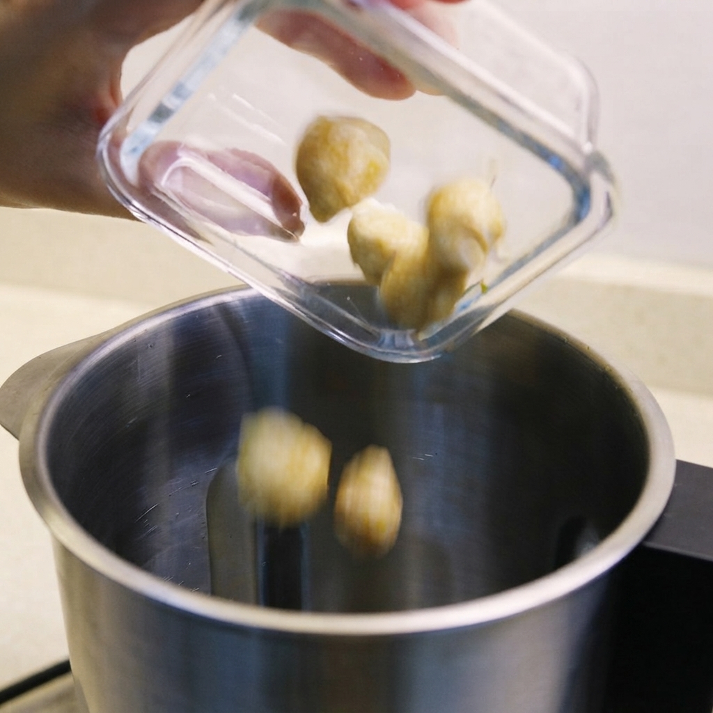 Noci candlenut, scalogni e belacan saltato versati nel contenitore di un frullatore.