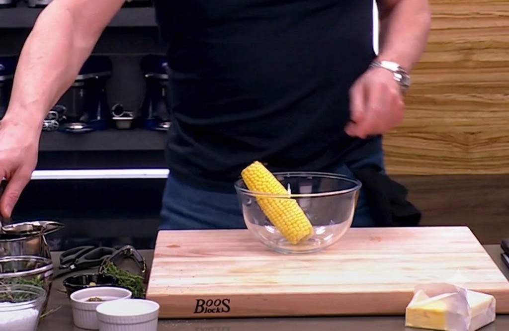 Una pannocchia di mais cruda in una ciotola di vetro, pronta per essere condita con olio doliva, sale e pepe.