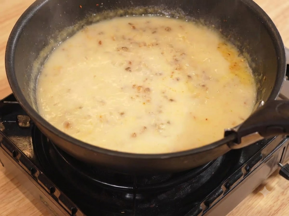 Acqua e latte versati nella padella con la miscela di curry, in cottura a fuoco lento.