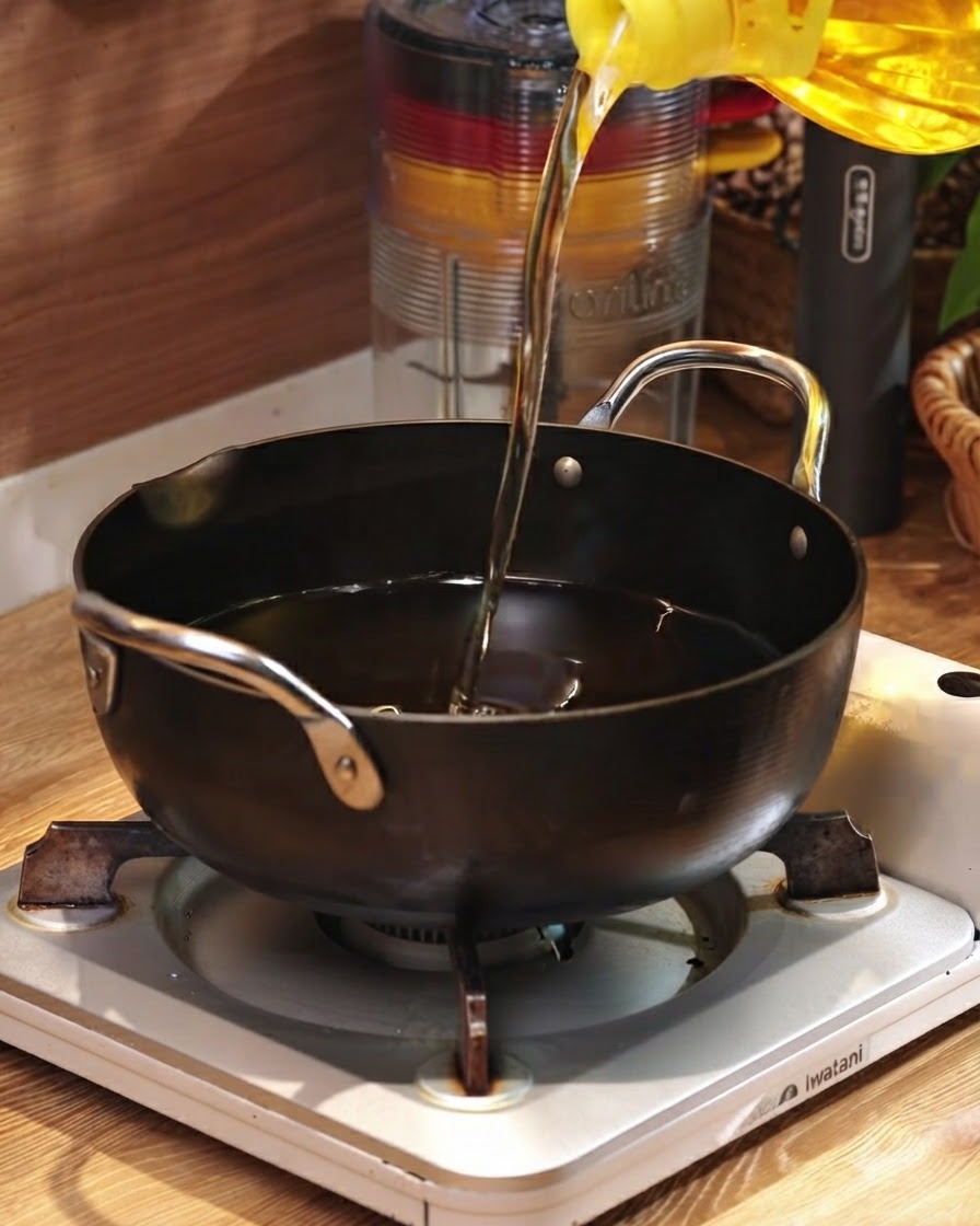 Olio da cucina versato da un contenitore giallo in una padella nera poggiata su un fornello portatile.