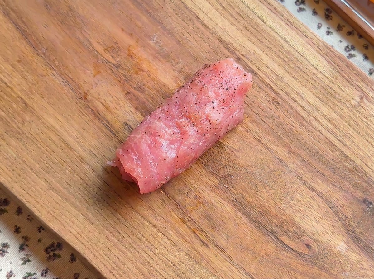 Un rotolo di cotoletta di maiale condita adagiato su un asse di legno.