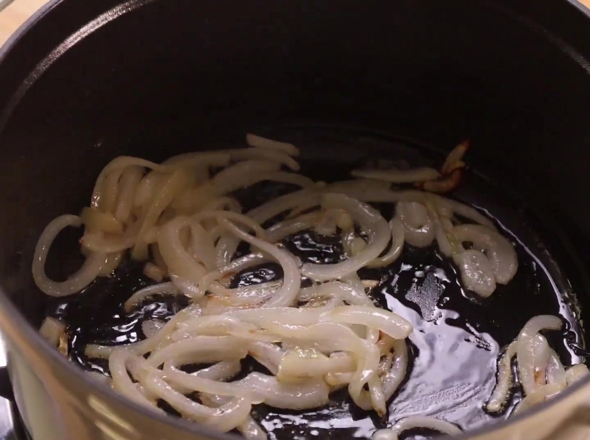 Cipolle che soffriggono nellolio sul fondo di una pentola scura.