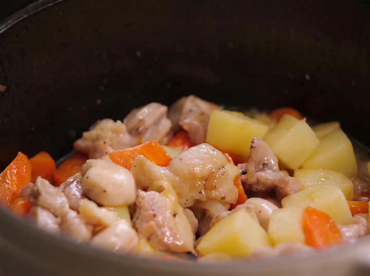 Pezzi di pollo fritti, pezzi di patata e pezzi di carota mescolati insieme allinterno di una pentola.
