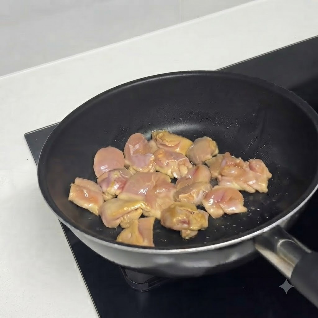 Pezzi di pollo marinato che sfrigolano in una padella calda oliata.
