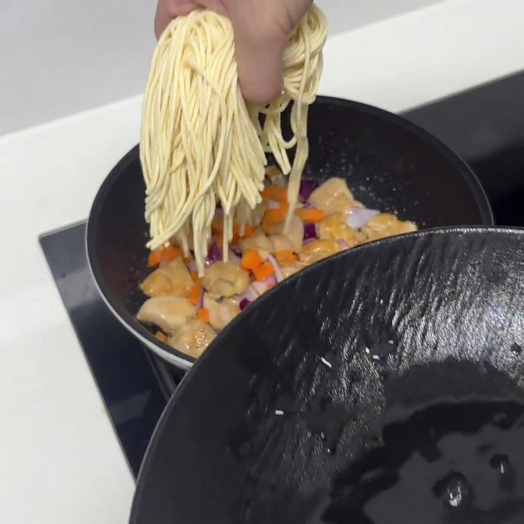 Noodles di pasta pre-ammollati aggiunti nella padella con pollo e verdure.