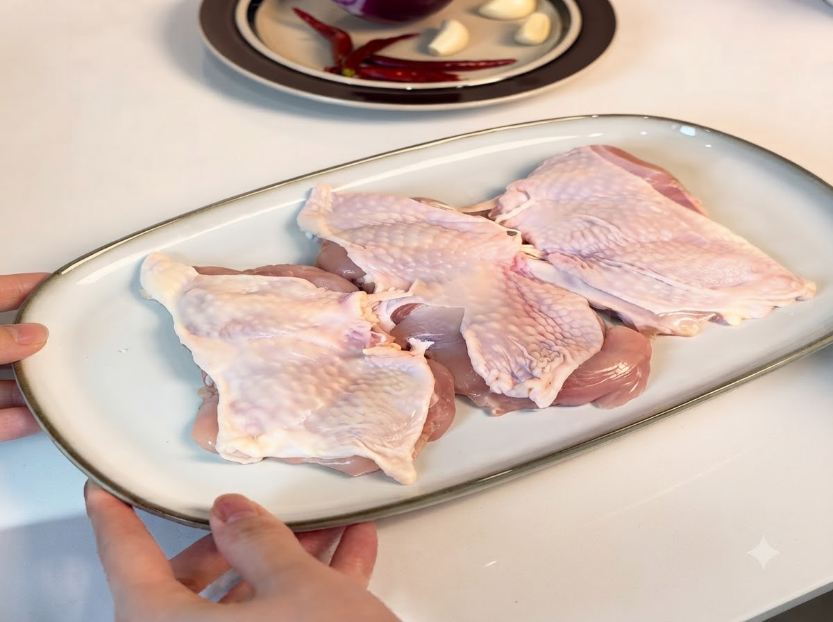 Cosce di pollo disossate disposte su un piatto da portata bianco, cosparse di condimenti.