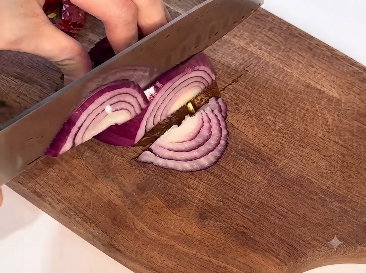 Una cipolla rossa affettata con cura su un tagliere di legno con un coltello.