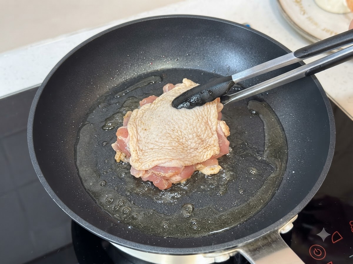 Una coscia di pollo condita che frigge dal lato della pelle in una padella calda unta dolio usando le pinze.