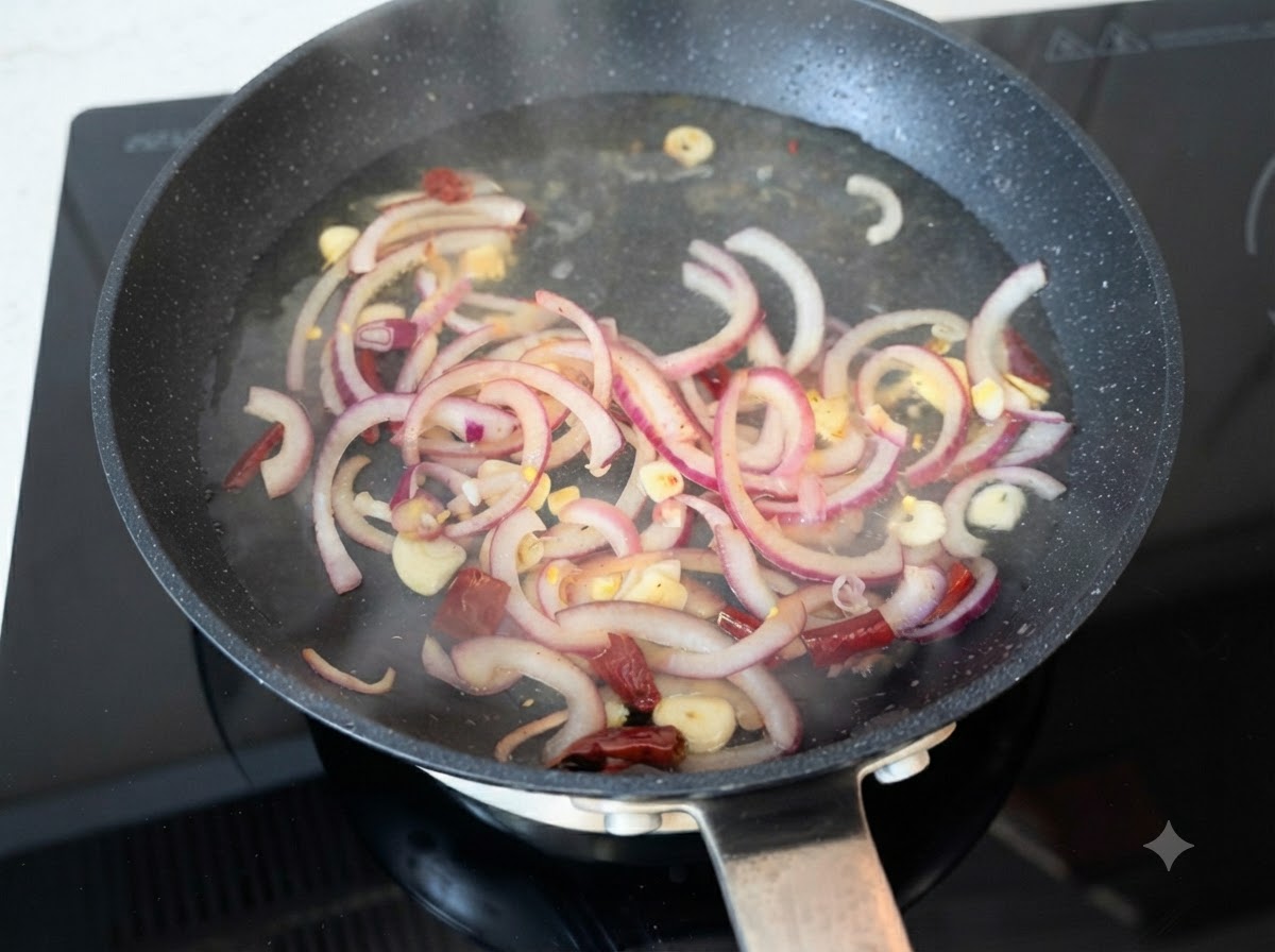 Acqua calda versata su fette di cipolla rossa rosolata, aglio e peperoncini in padella.