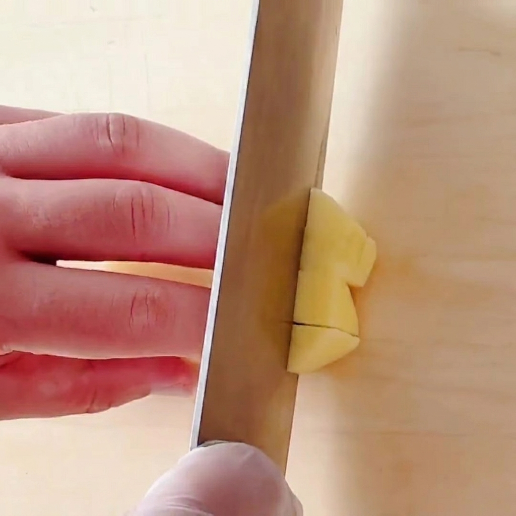 Patate tagliate a piccoli cubetti quadrati su un tagliere di legno.