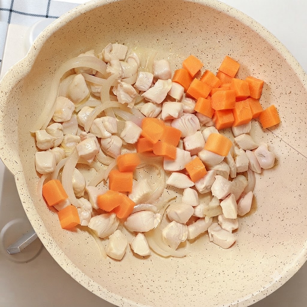 Cubetti di carota arancione vivace aggiunti alla padella contenente pollo e cipolle.