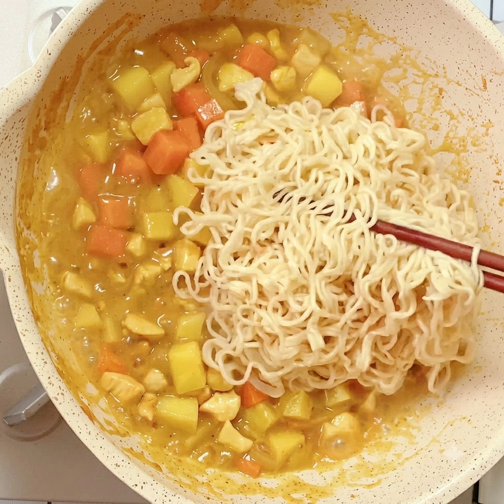 Noodle istantanei precotti inseriti con le bacchette in una padella con la miscela di curry in riduzione.