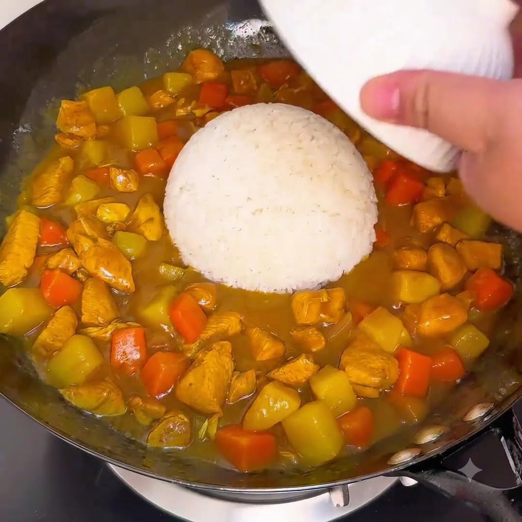 Una ciotola di riso bianco rovesciata direttamente nella salsa al curry in ebollizione in un wok.