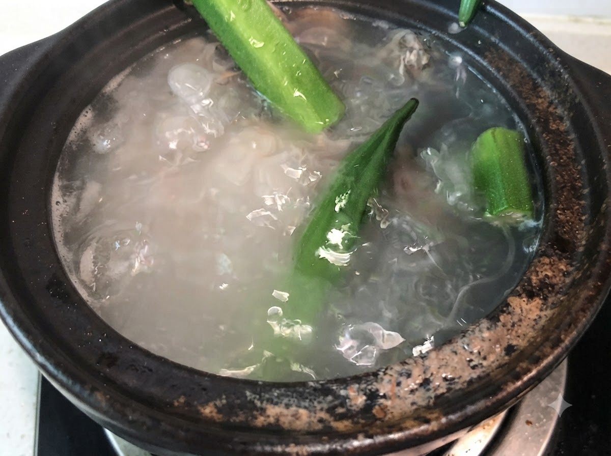 Interi baccelli di okra verde aggiunti nel brodo di ossa di maiale in ebollizione.