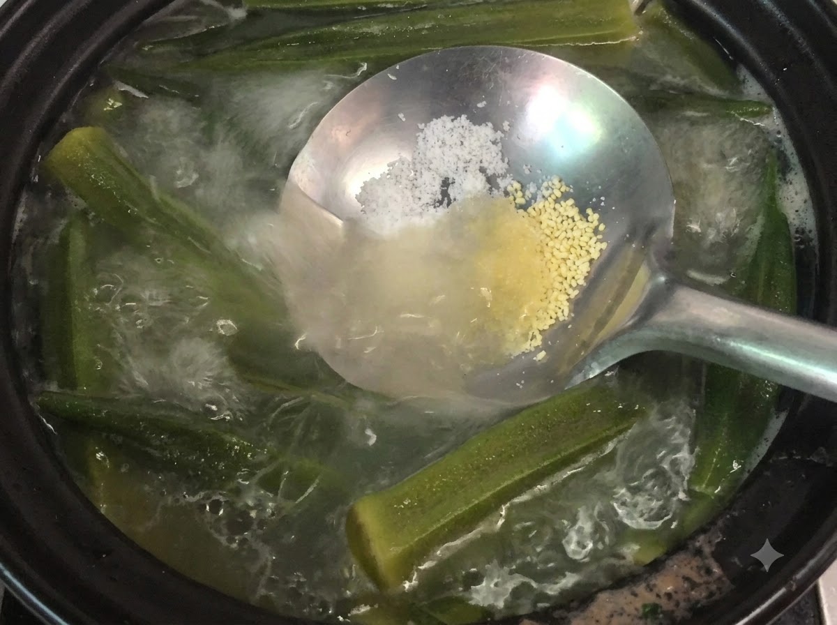 Un mestolo che tiene sale e polvere di pollo sopra una pentola fumante di zuppa di okra e ossa.