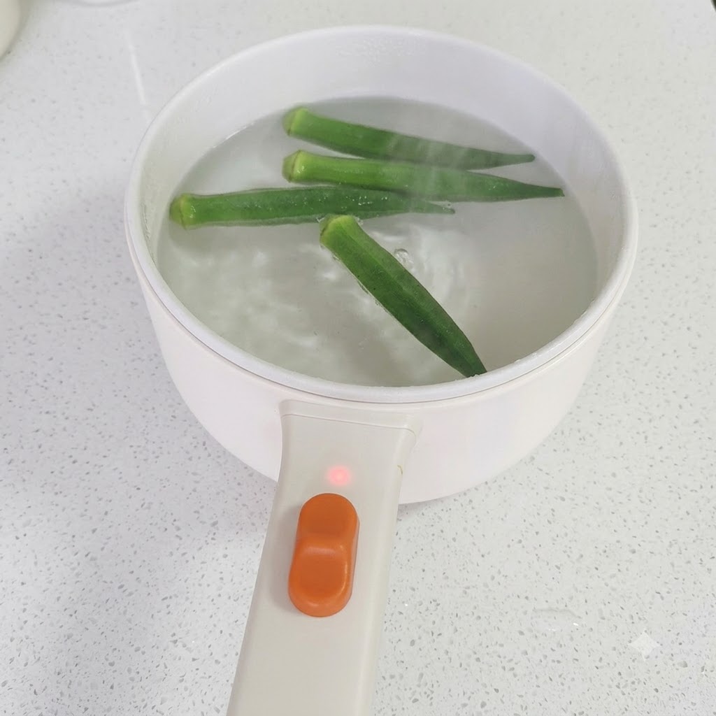 Bacchette che sollevano lokra verde cotta da una pentola di acqua in ebollizione.