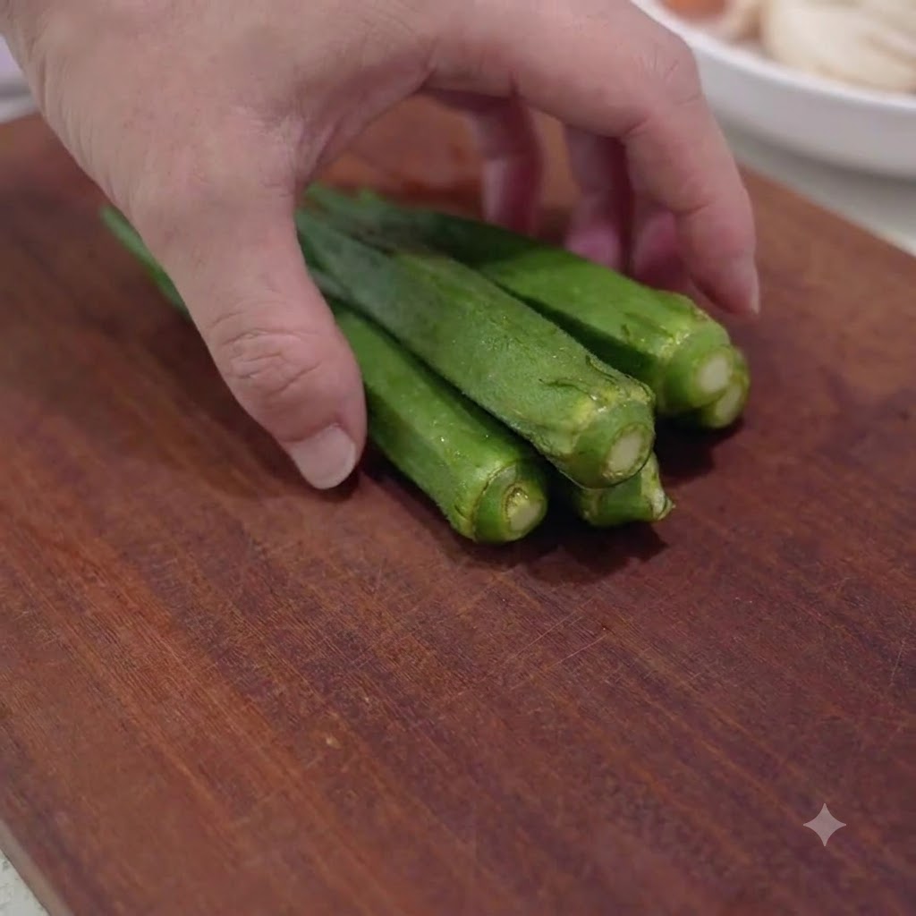 Baccelli di okra verde fresca tagliati a piccoli pezzi su un tagliere di legno.