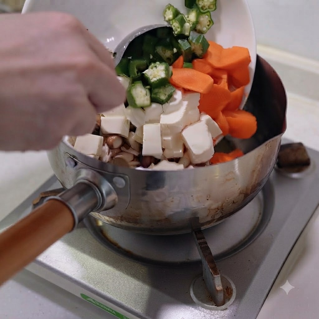 Verdure tagliate e tofu trasferiti da un piatto bianco in una pentola di acciaio inossidabile.