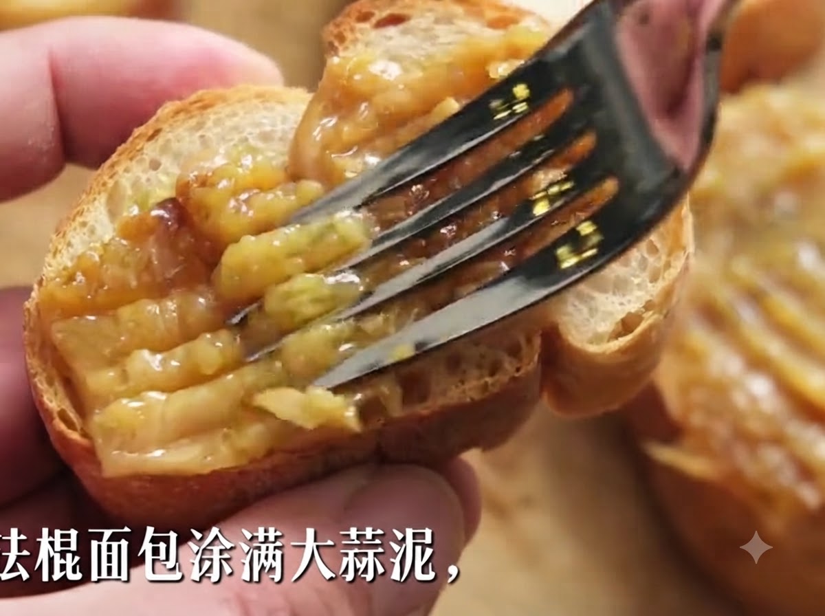 Una forchetta che spalma densa pasta di aglio arrostito su una fetta di baguette croccante.