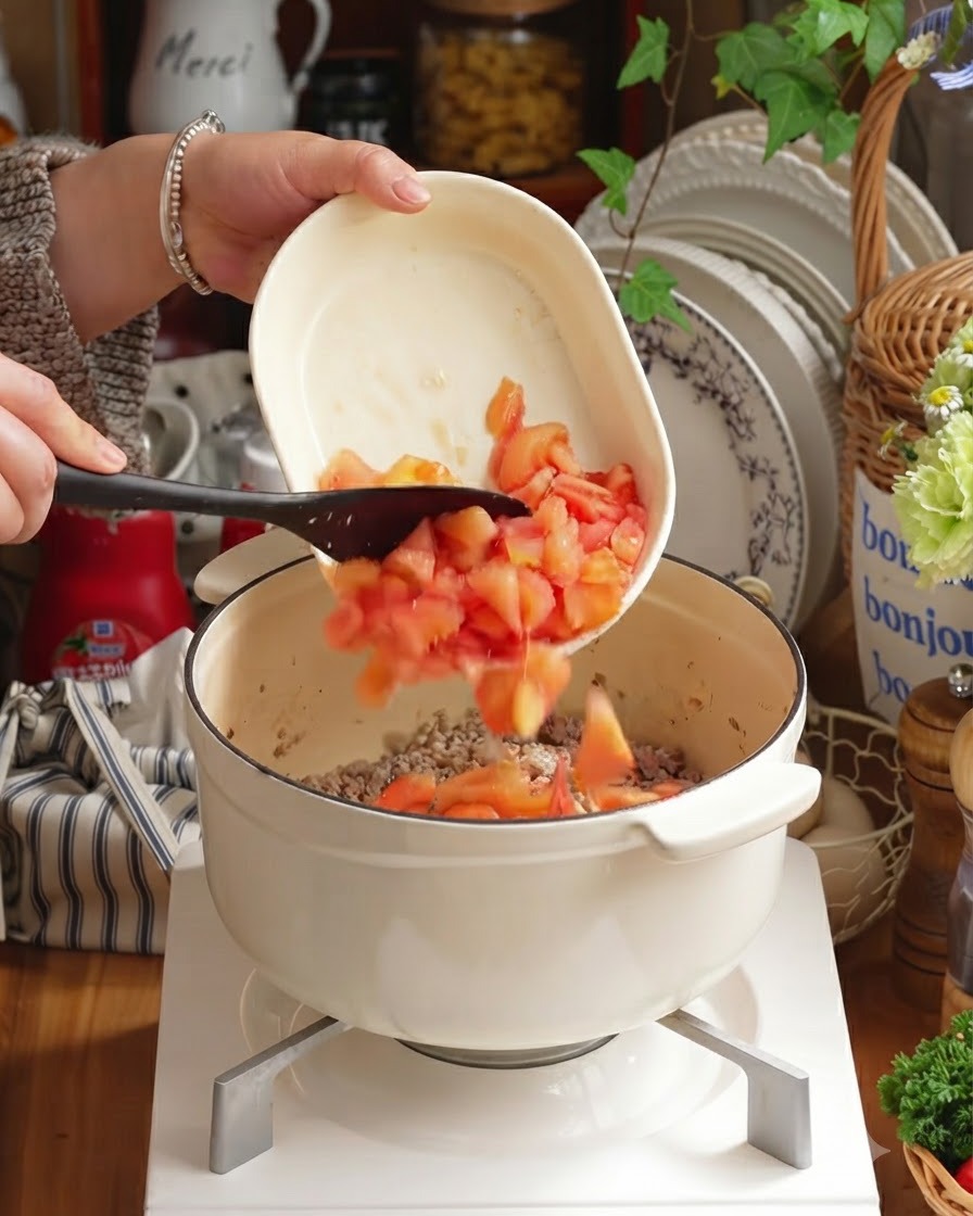 Pomodori pelati a cubetti e verdure tritate aggiunti nella pentola sopra la carne.