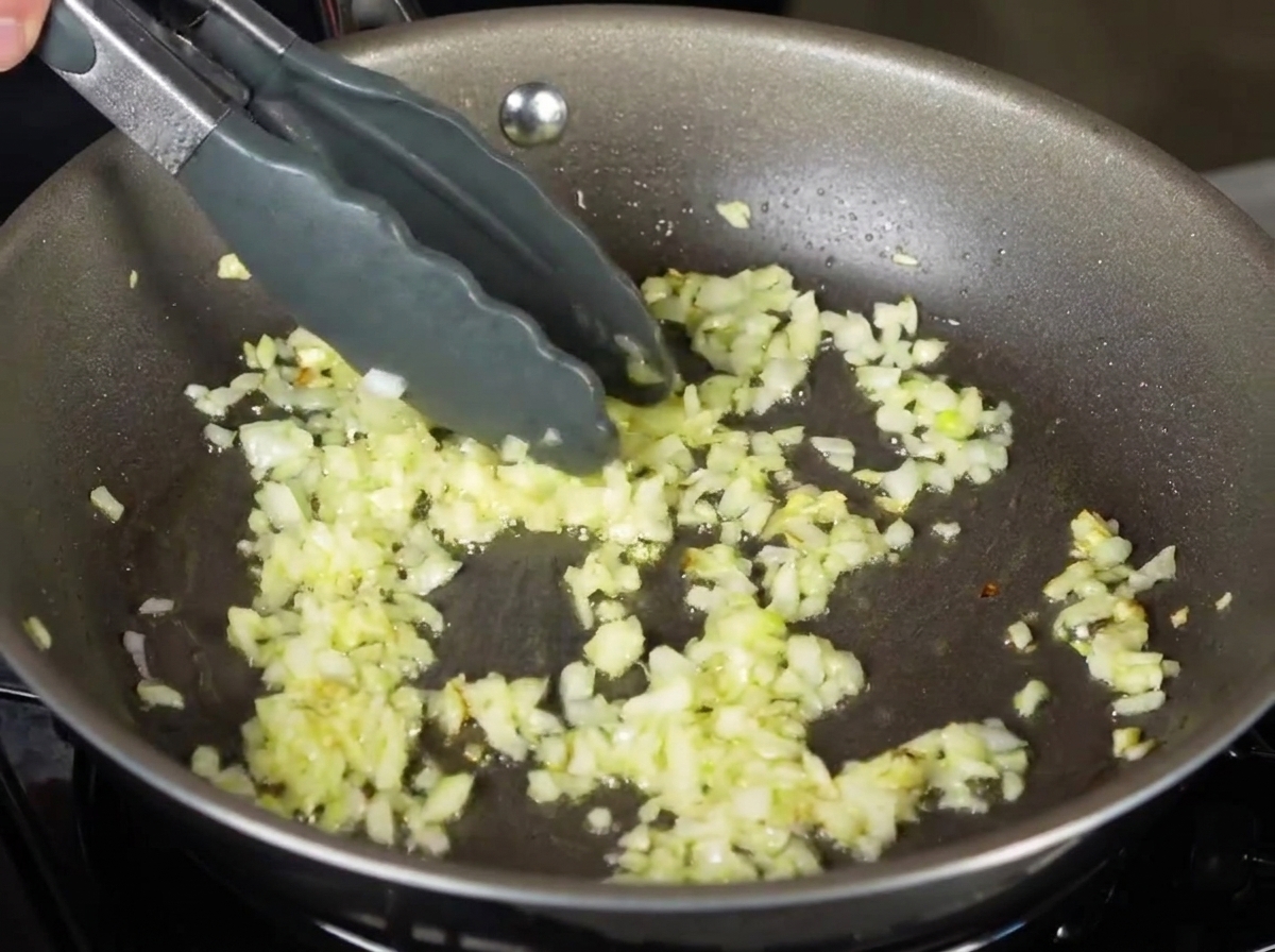 Tagliatelle bollite messe con le pinze in una padella con cipolle tritate e soffritte.