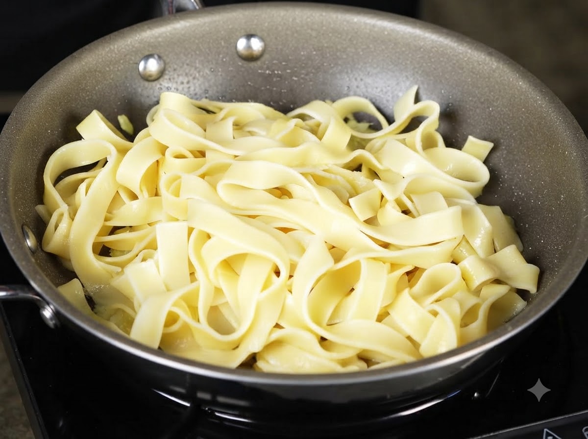 Un mestolo che raccoglie e versa lacqua amidacea della pasta sui noodles allinterno della padella.