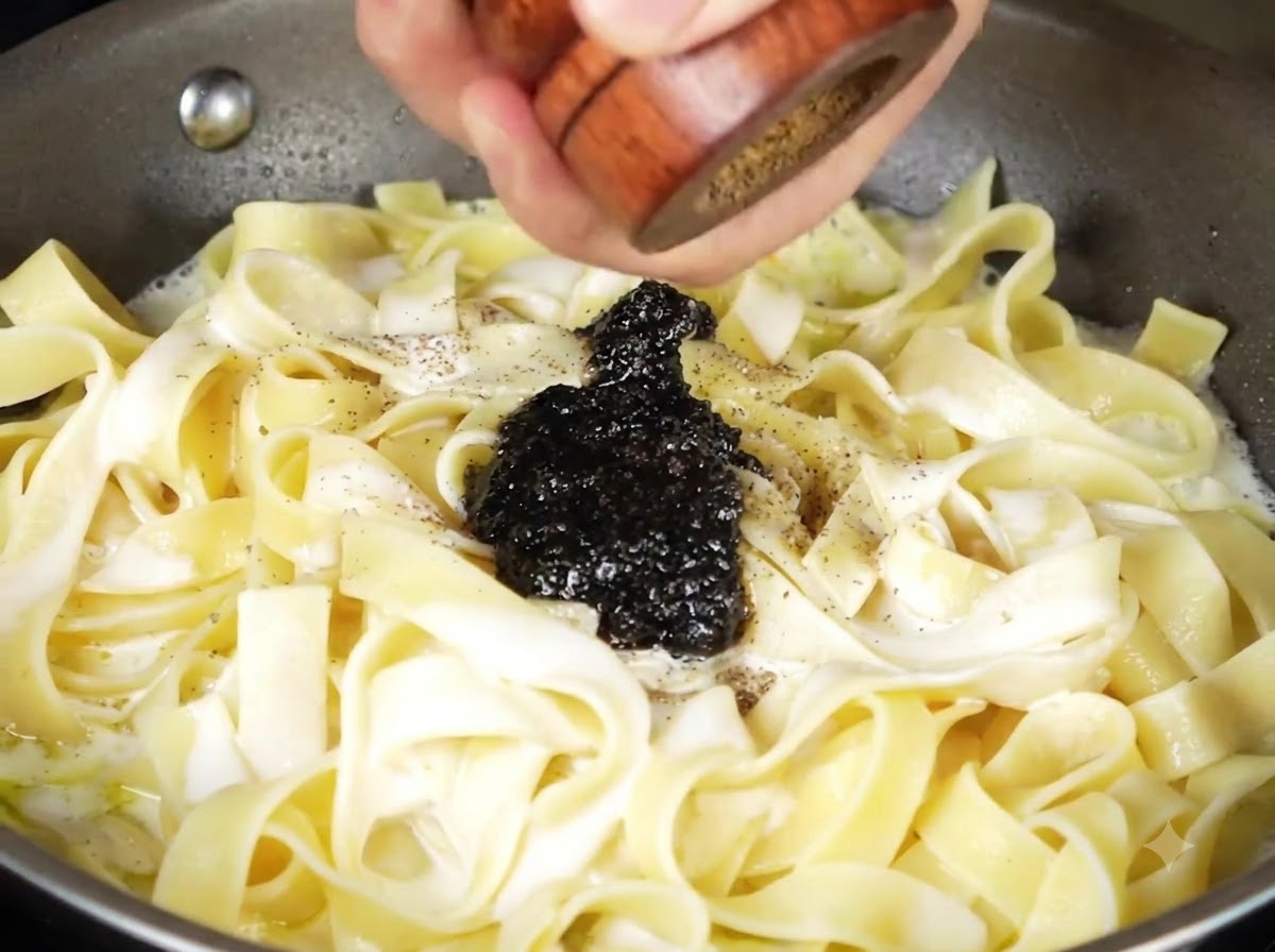 Salsa di tartufo nero e pepe nero macinato fresco sopra la pasta cremosa nella padella.