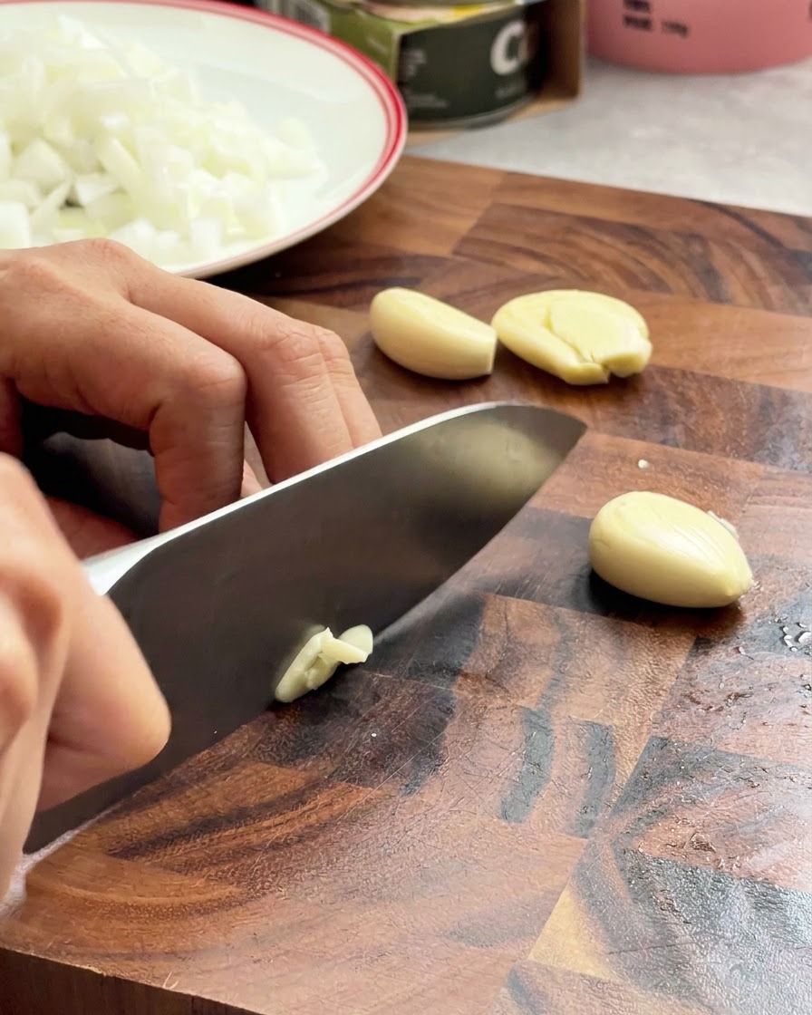 Spicchi daglio tritati con un coltello da chef su una superficie di legno.