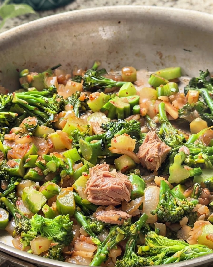 Pezzi di tonno in scatola mescolati nella padella con broccoli verdi e cipolle.