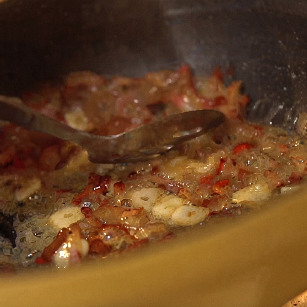 Pomodori pelati in scatola mescolati agli ingredienti della padella sfrigolante con un cucchiaio.