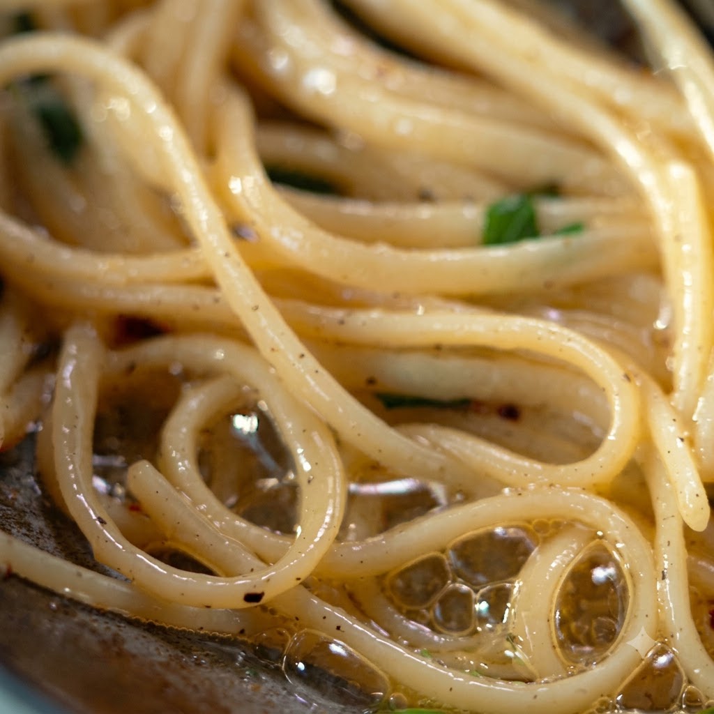 Un mestolo e delle pinze che sollevano e trasferiscono la pasta condita su un piatto dargento.
