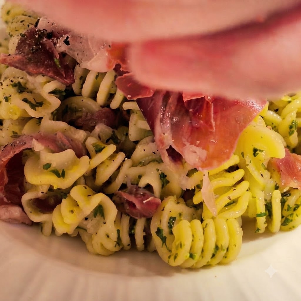Pasta a spirale appena cotta trasferita nella ciotola con la salsa di burro e aglio preparata, guarnita con erbe fresche e prosciutto.