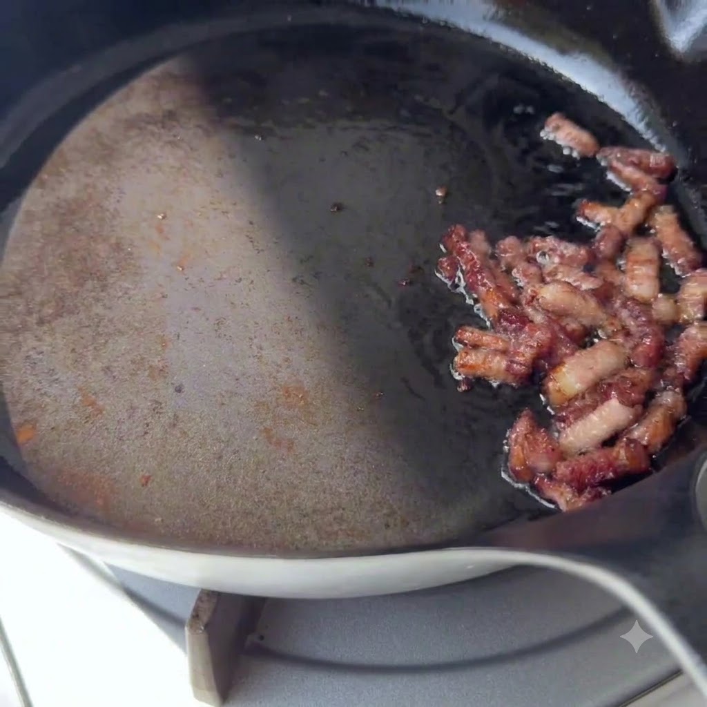 Pezzi di pancetta dorati che sfrigolano su un lato di una padella calda.