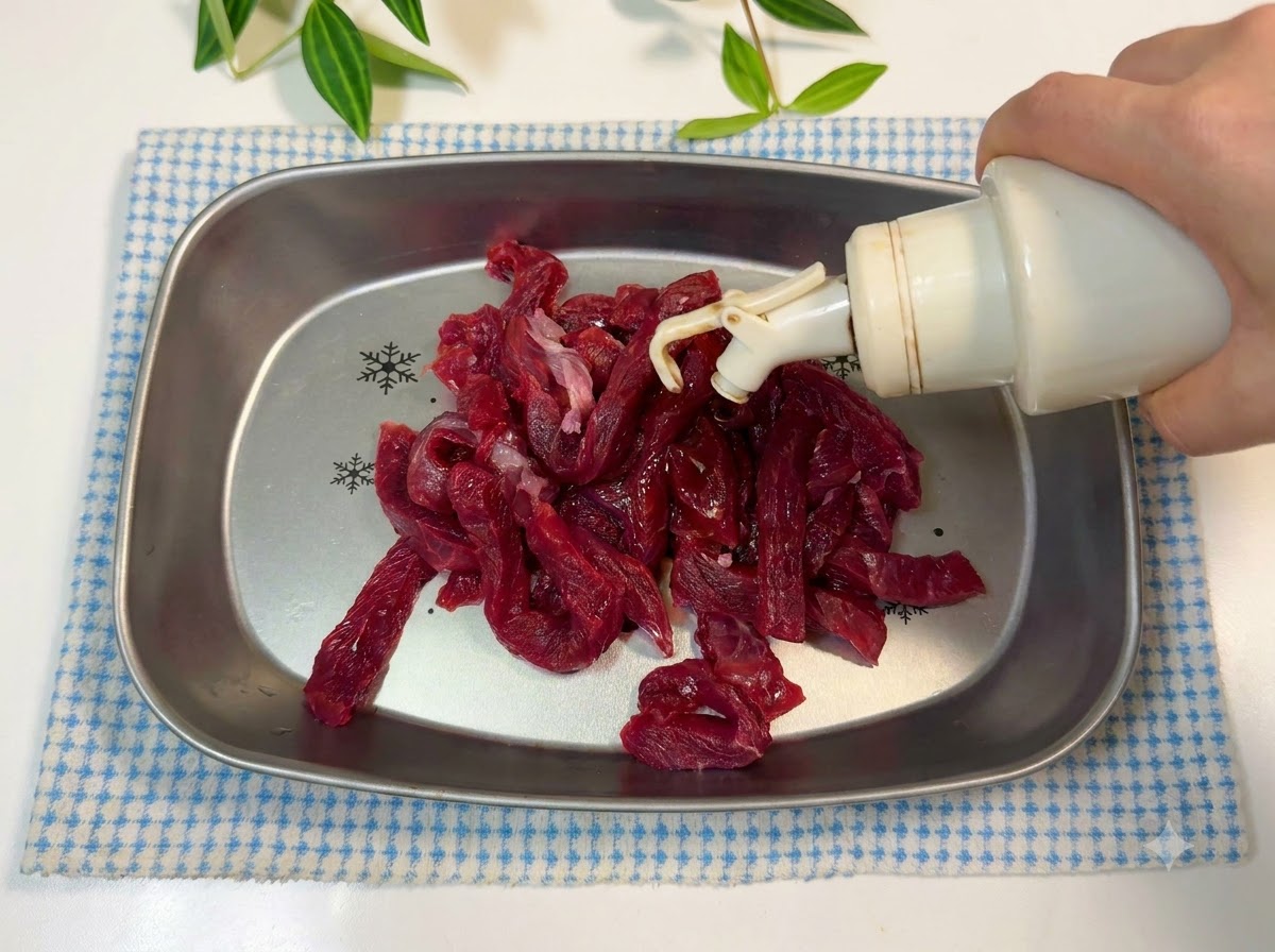 Strisce di manzo in una teglia di metallo condite con olio e salsa di soia.