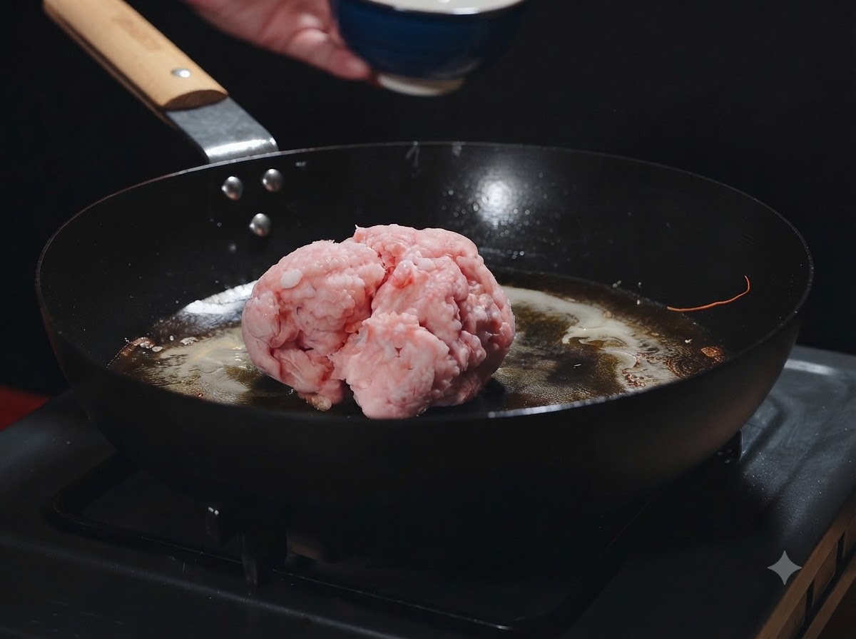 Una palla di carne macinata cruda che viene aggiunta in una padella calda con olio di gamberi.