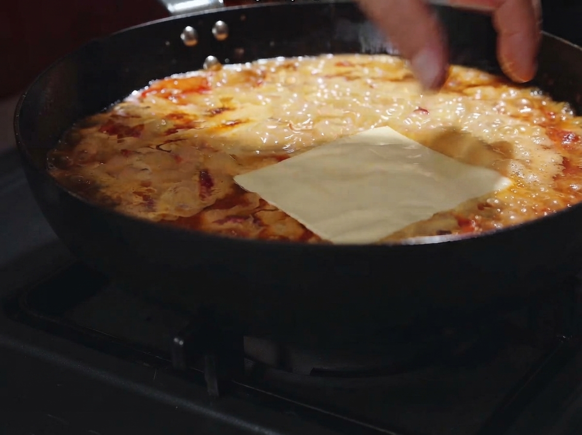 Una fetta di formaggio appoggiata sul sugo cremoso gorgogliante nella padella.