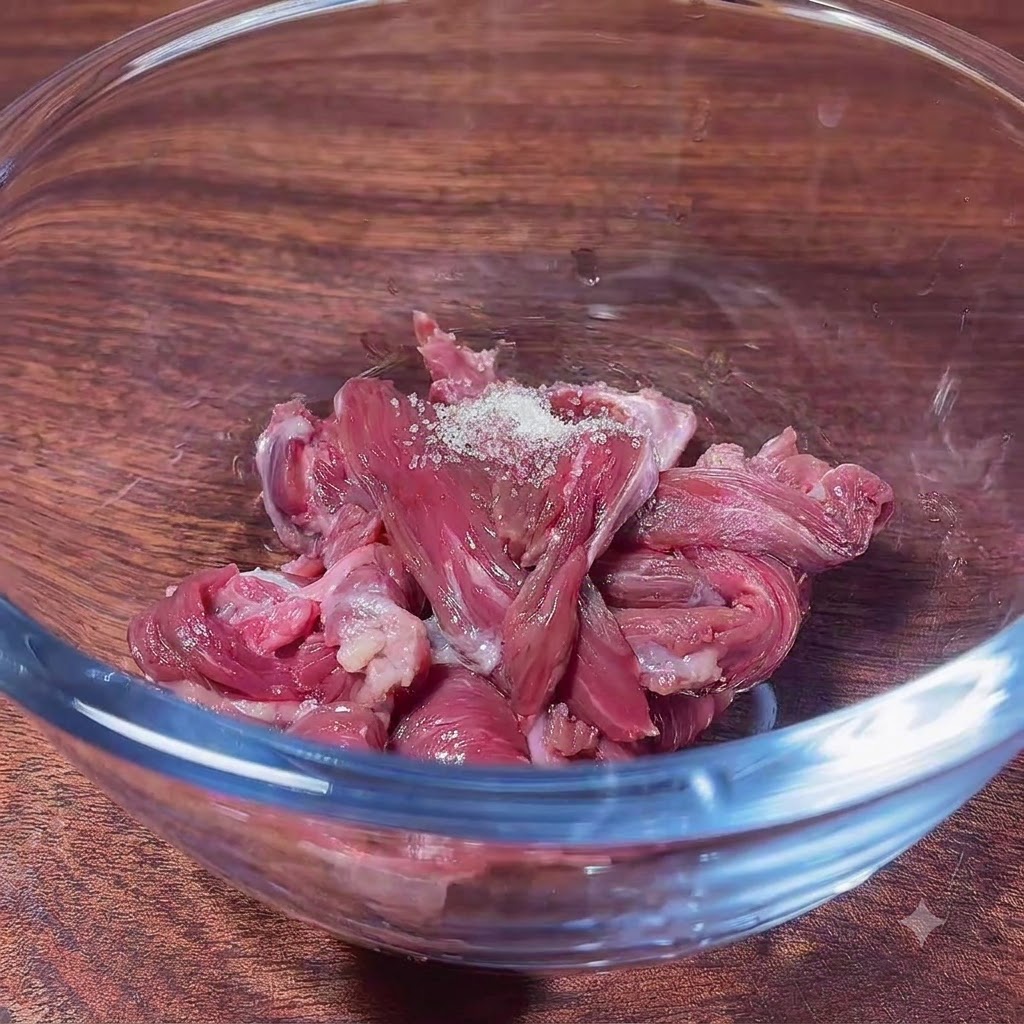 Fettine di manzo crudo in una ciotola di vetro con zucchero, pronte per essere mescolate agli ingredienti della marinatura.