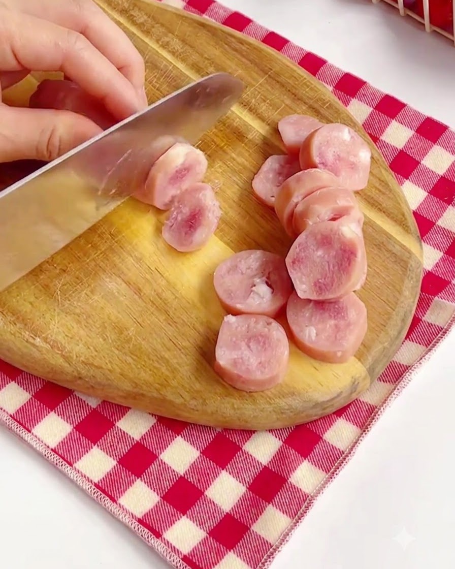 Taglio di salsicce rosa in pezzi rotondi su un tagliere di legno.