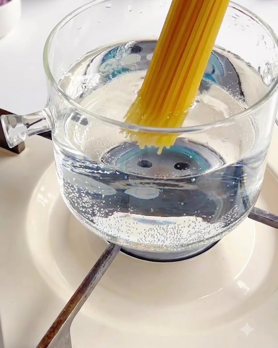 Inserimento di un fascio di spaghetti secchi in una pentola di vetro bollente con acqua calda.