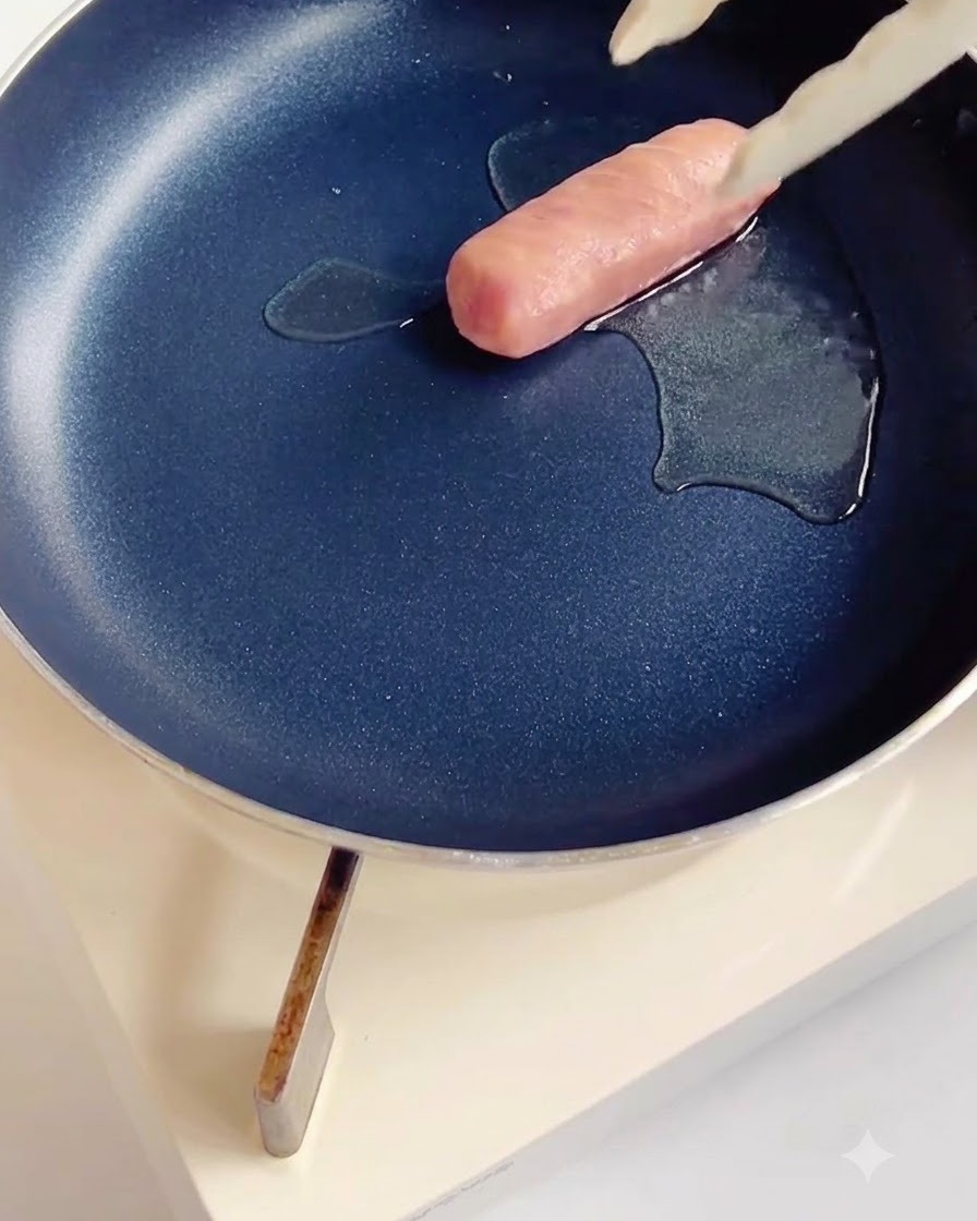 Salsiccia incisa che frigge in una padella antiaderente scura con una piccola quantità di olio.