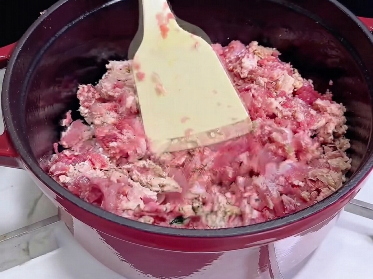 Utilizzo di una spatola bianca per saltare la carne macinata in una pentola di ghisa rossa mentre inizia a dorarsi.