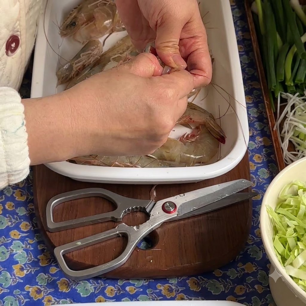 Mani che sbucciano e rimuovono la vena scura da un gambero crudo su un vassoio bianco.