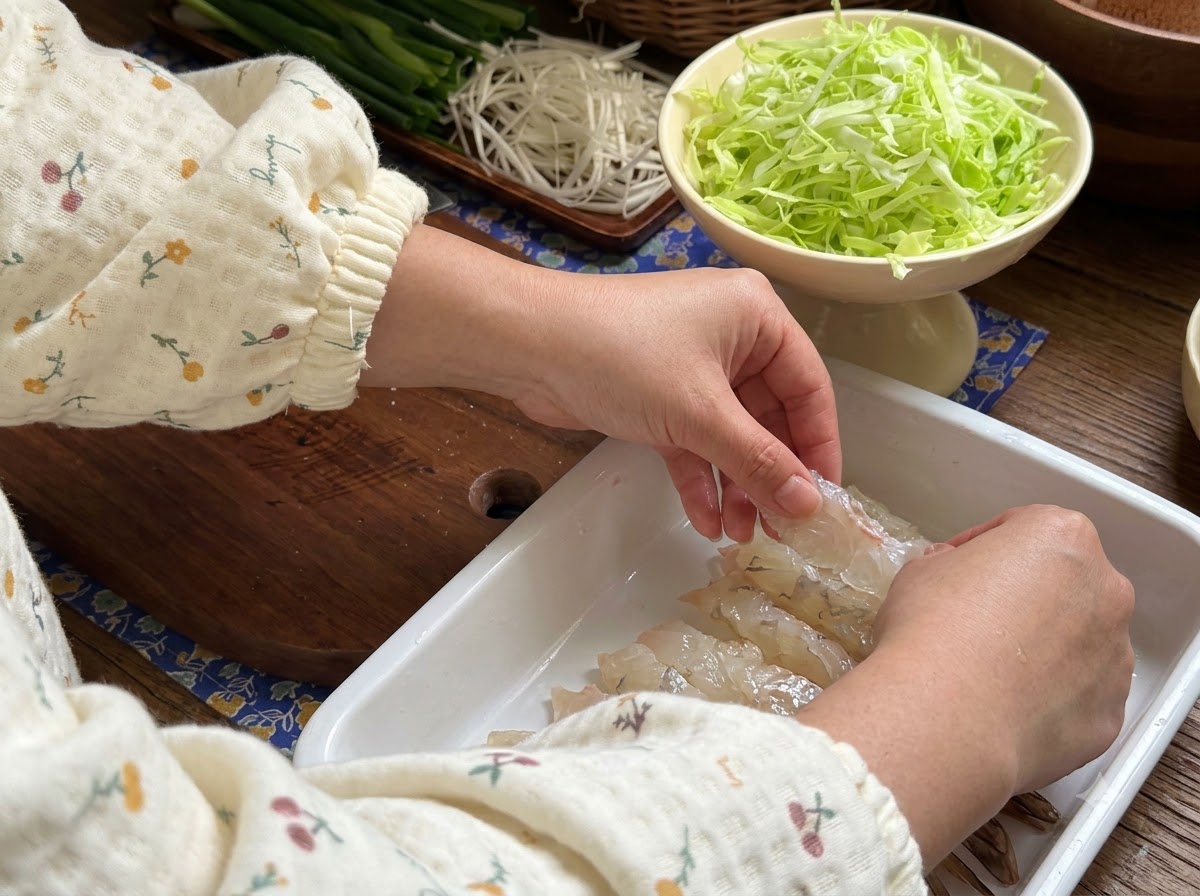 Mani che premono i gamberi crudi piatti in un vassoio bianco per prepararli alla marinatura.