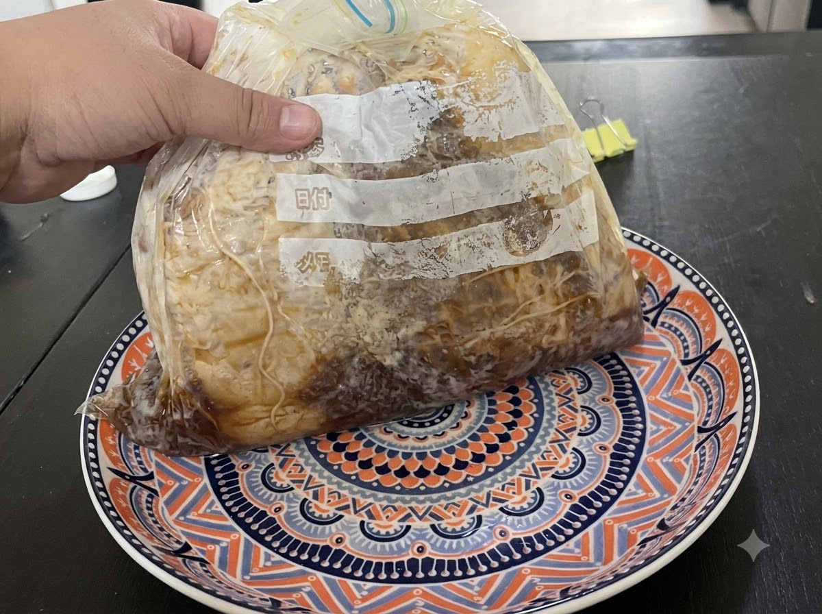 Una mano che regge una busta sottovuoto di carne marinata poggiata su un piatto decorato.