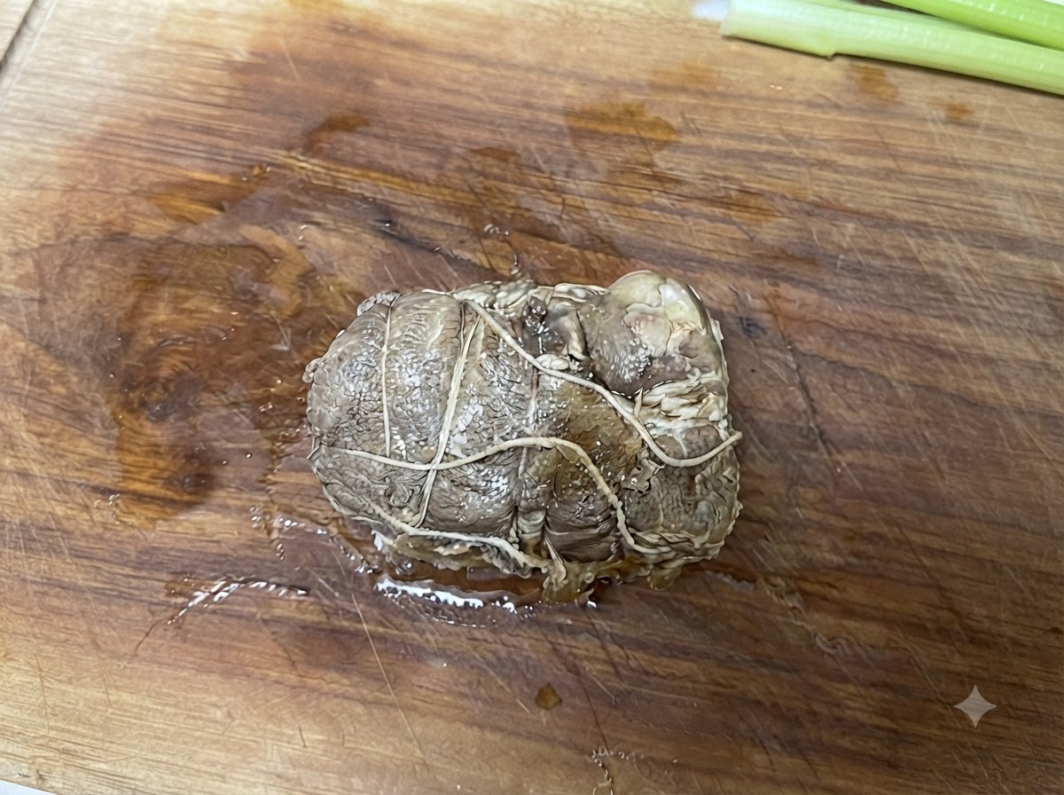 Chashu di maiale arrotolato e legato poggiato su un tagliere di legno prima di essere affettato.