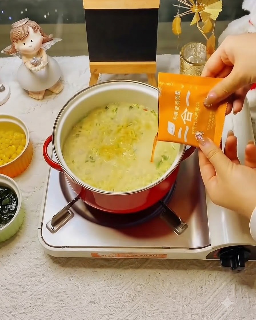 Una bustina di condimento per zuppa arancione che viene versata nella pentola di noodles in ebollizione.