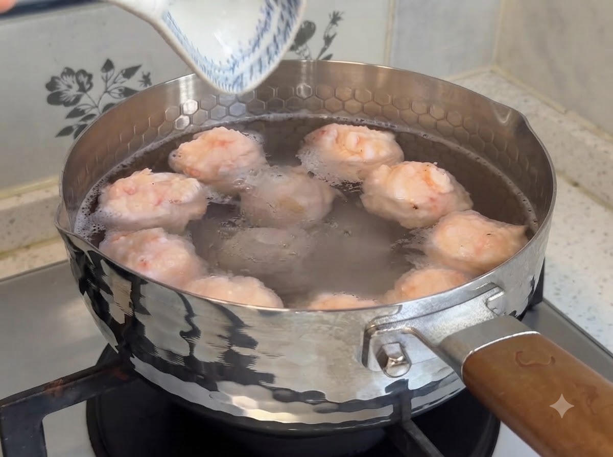 Polpette di gamberi fatte in casa che sobbollono in una pentola di acqua calda sul fuoco.