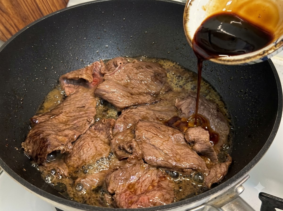 Salsa teriyaki versata in una padella sopra fette di manzo grasso mentre sobbollono e si riducono.
